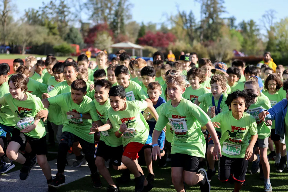 a large group of young boys running in a race outside wearing green t-shirts