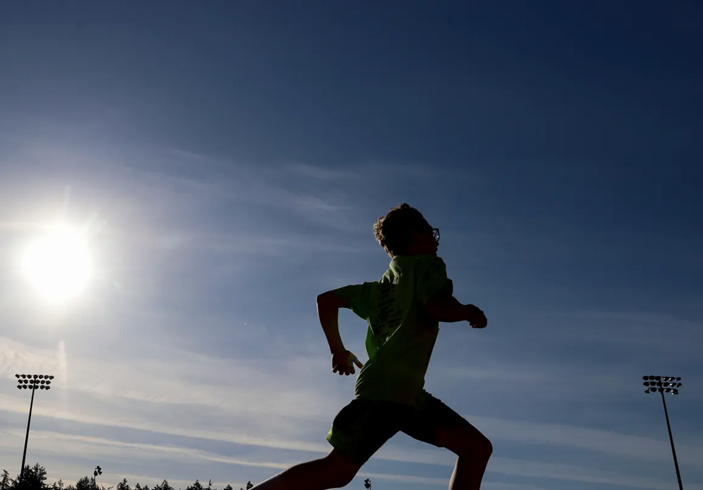 an upward angle of a kid running outside with a blue sky, sun, and flood lights