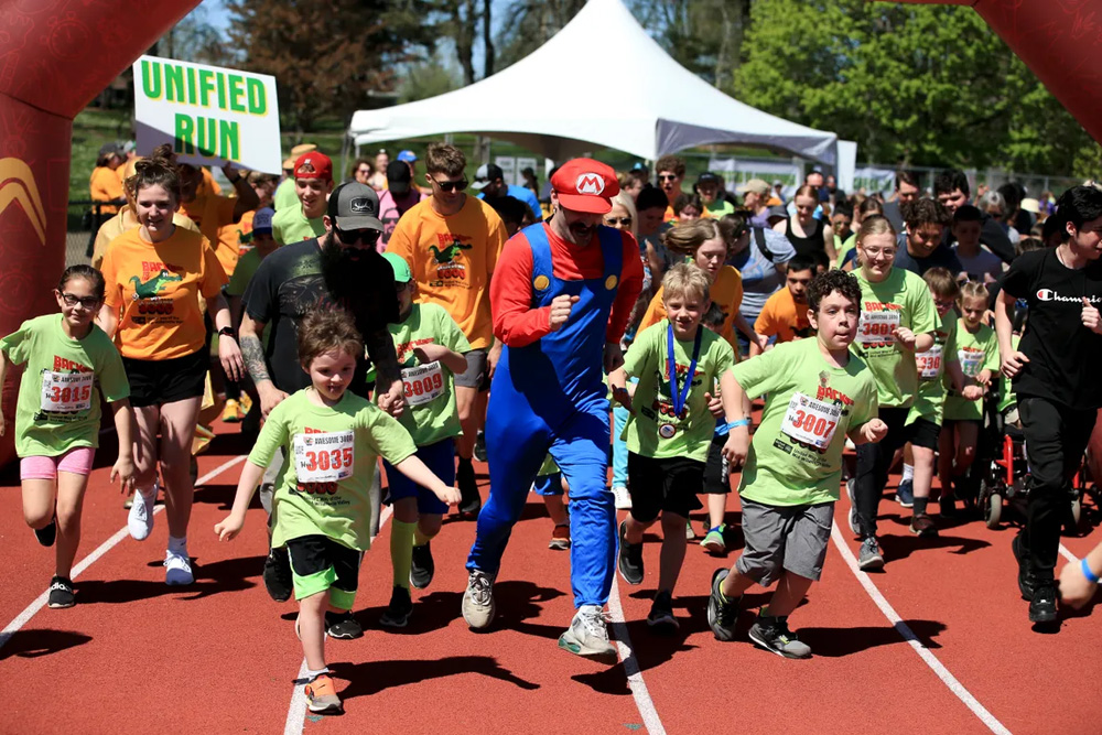 A man dressed up like Mario running a race with a large group of kids and teens