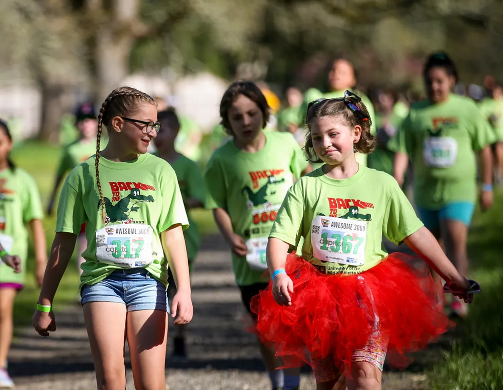 two girls in focus, kids blurry in the background, participating in the race wearing green t-shirts