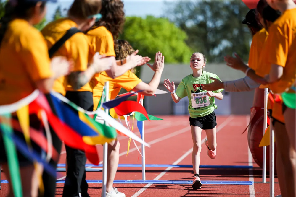a girl crossing the finish line in a green t-shirt and black shorts, giving high fives to the crown on each side of her