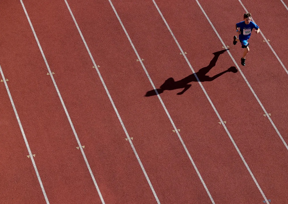 Ariel shot of a boy running alone on a track wearing all blue and his shadow